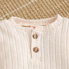 A close-up of a light pink knitted baby romper top with a button placket and ribbed texture.