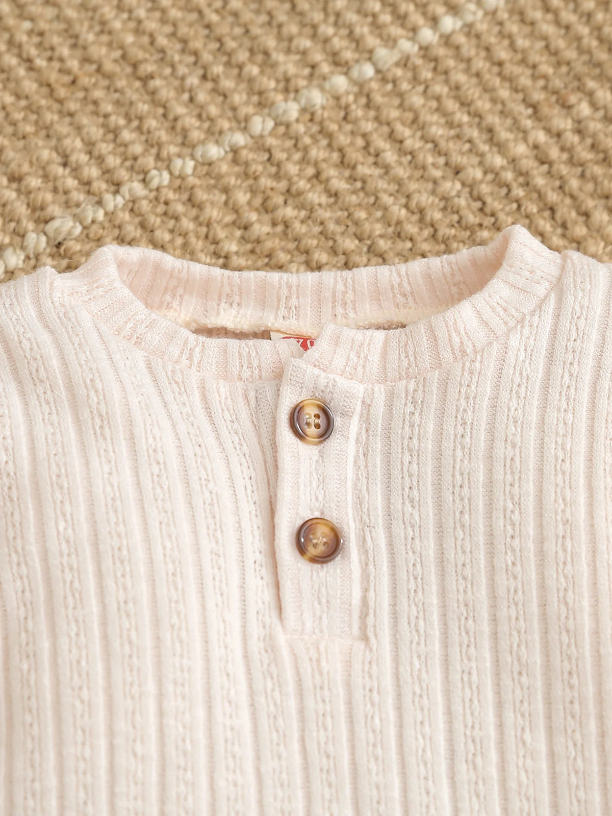 A close-up of a light pink knitted baby romper top with a button placket and ribbed texture.