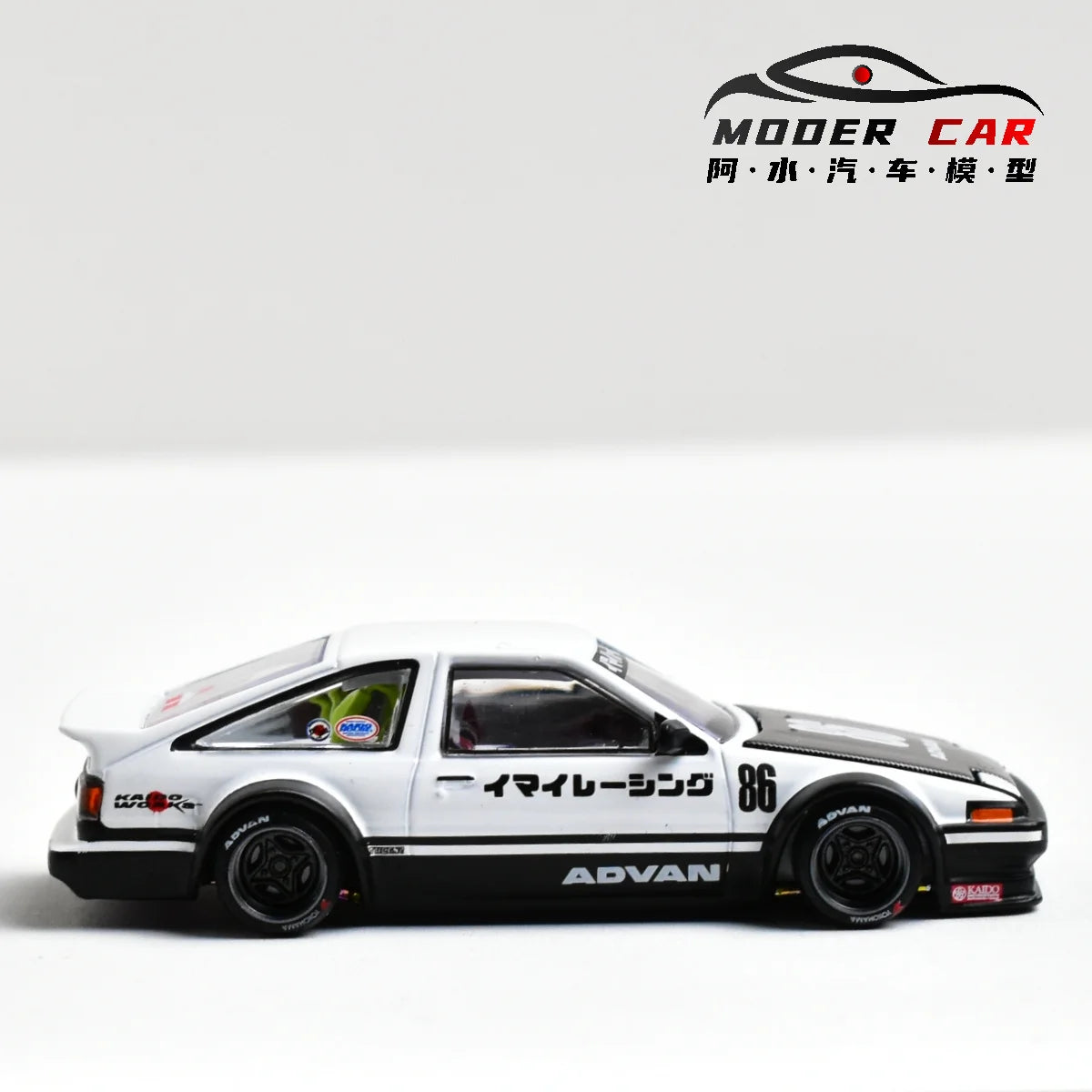 A white and black diecast model of a Toyota AE86 car with racing decals displayed on a white background.