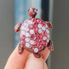 A detailed rhinestone turtle brooch pin with pink and clear stones is held in a hand.