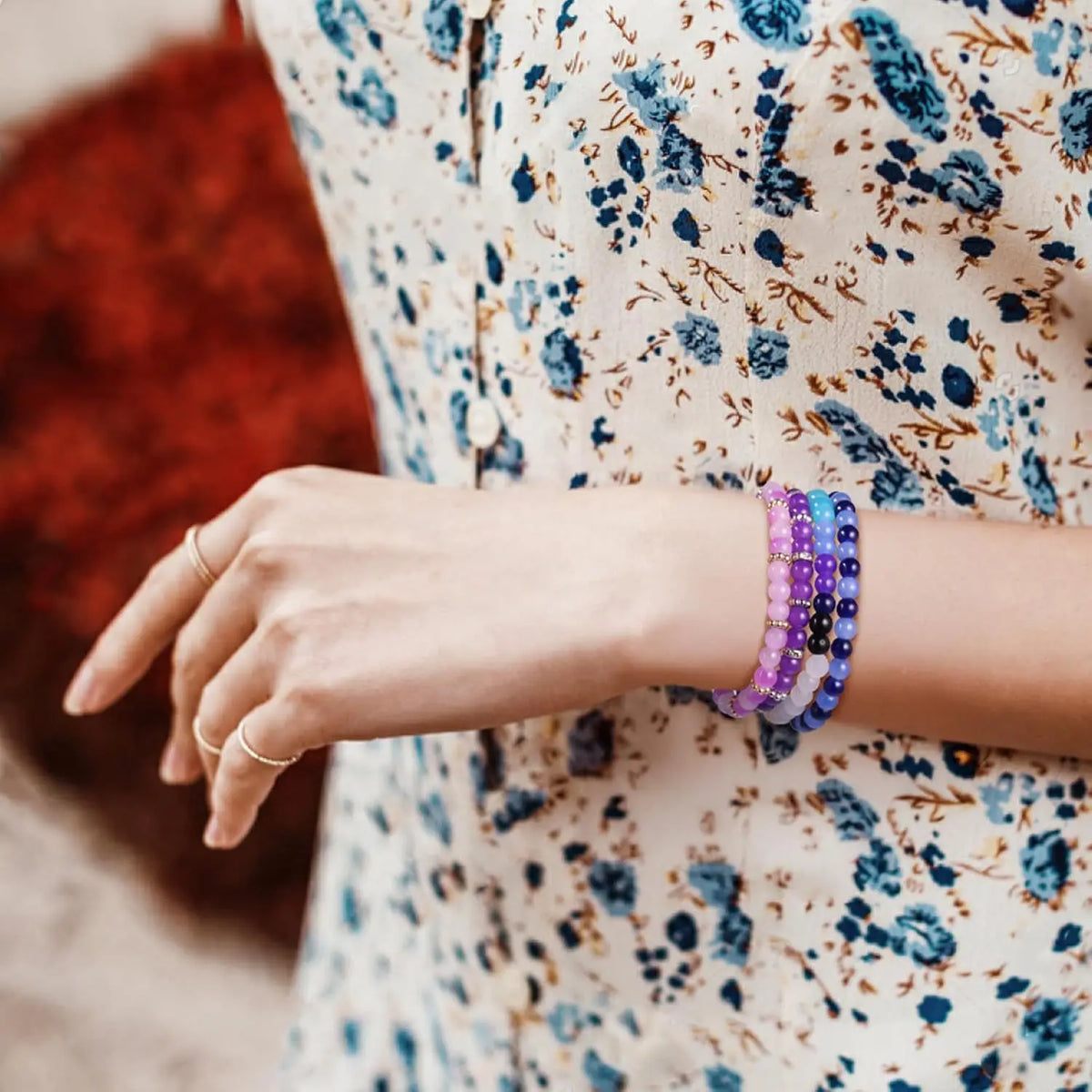 A hand wearing a stack of purple glass beads for jewelry making against a floral patterned fabric.