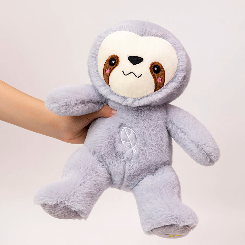 A hand is holding a soft, gray sloth plush toy with a light-colored face and a symbol on its chest.