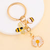Gold-toned enamel keychain featuring a bee and a daisy flower design.