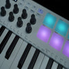 Close-up view of a portable MIDI keyboard controller with black keys and illuminated blue and purple drum pads.