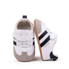 A pair of white and black baby first walkers shoes with soft soles shown from the side.