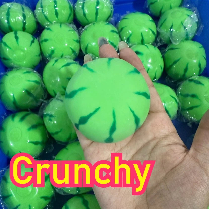 A hand holds a bright green watermelon squishy stress ball with a textured surface.