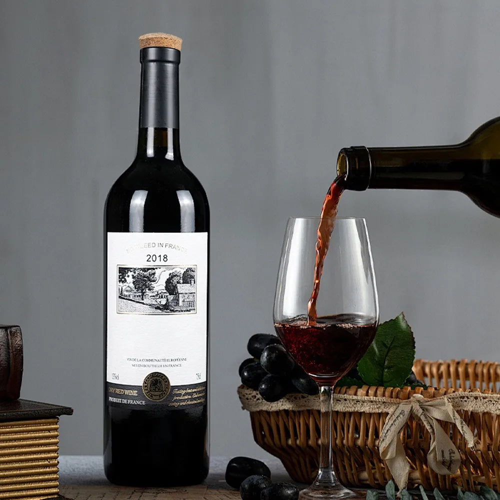 A dark glass bottle of red wine is being poured into a wine glass, with grapes and a wooden crate in the background.