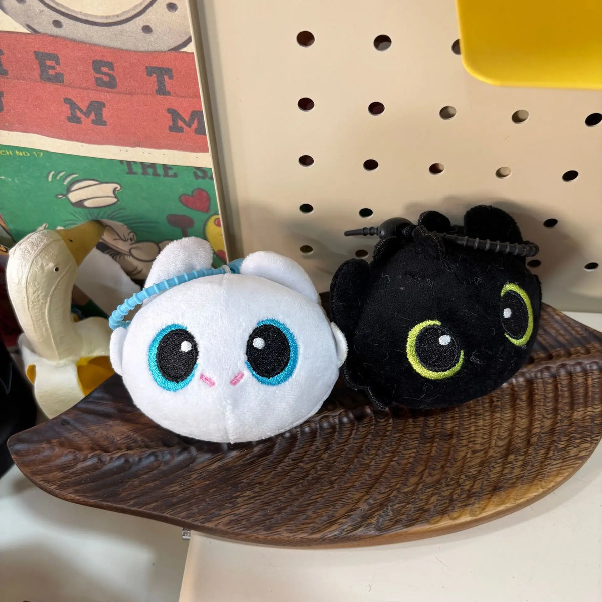 A white and light blue cartoon plush doll resembling Toothless, resting on a dark wooden surface.