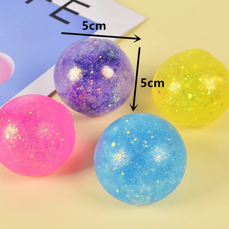 A collection of five colorful, glittery, spherical squeeze toys in pink, purple, yellow, and blue are displayed on a light su
