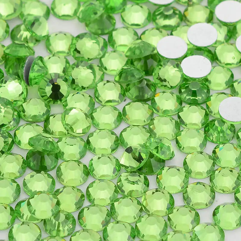 Green glass crystal flatback rhinestones for nail art and crafts scattered on a white surface