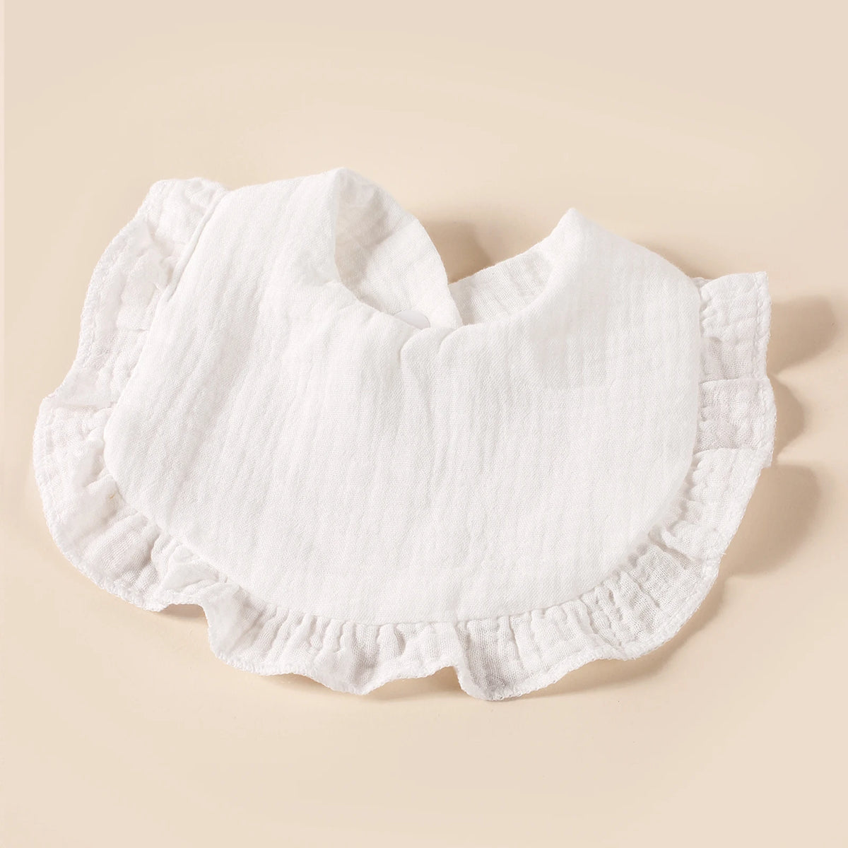 A set of eight white cotton ruffle baby bibs laid flat on a light beige background.