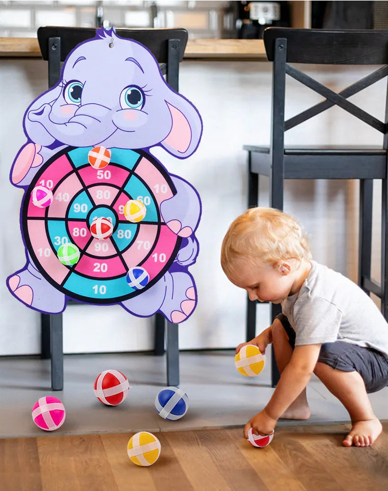 A purple elephant character holding a colorful dart board with sticky balls on a wooden floor.