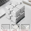 Cube anti-stress en métal argenté à coins arrondis sur un bureau blanc.
