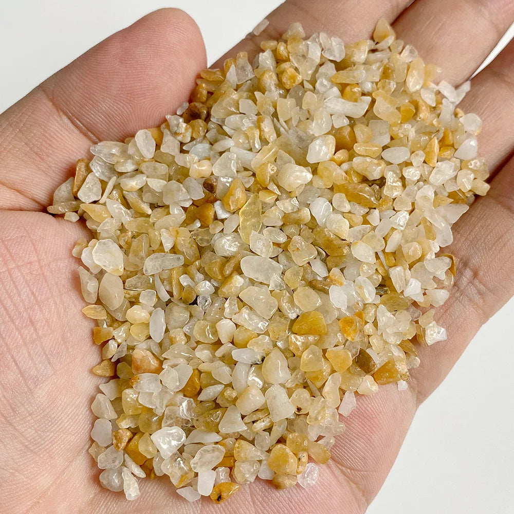 A hand holds a pile of natural tumbled stone chips in shades of yellow and clear quartz for jewelry making or home decor.