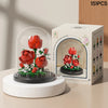 A white glass building block flower garden display featuring red roses and greenery, packaged in a box.