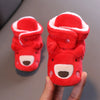 A pair of red animal-themed baby first walker shoes with white trim being held in a hand.
