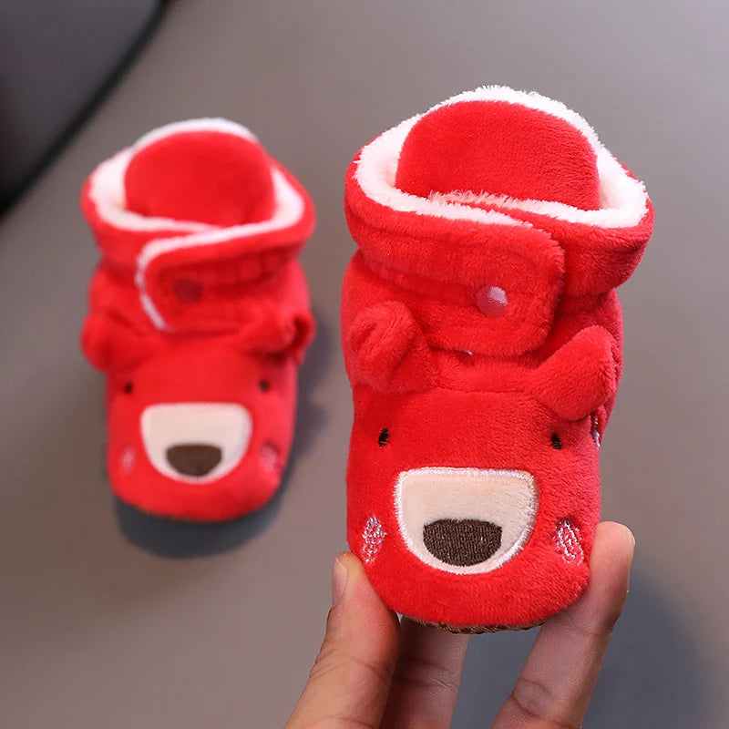 A pair of red animal-themed baby first walker shoes with white trim being held in a hand.