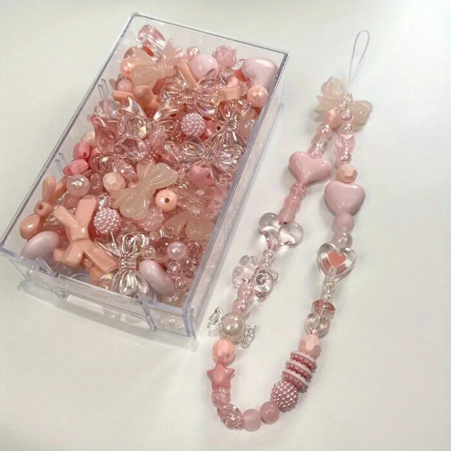 A clear box filled with pink and translucent acrylic loose beads for jewelry making, alongside a string of matching beads.