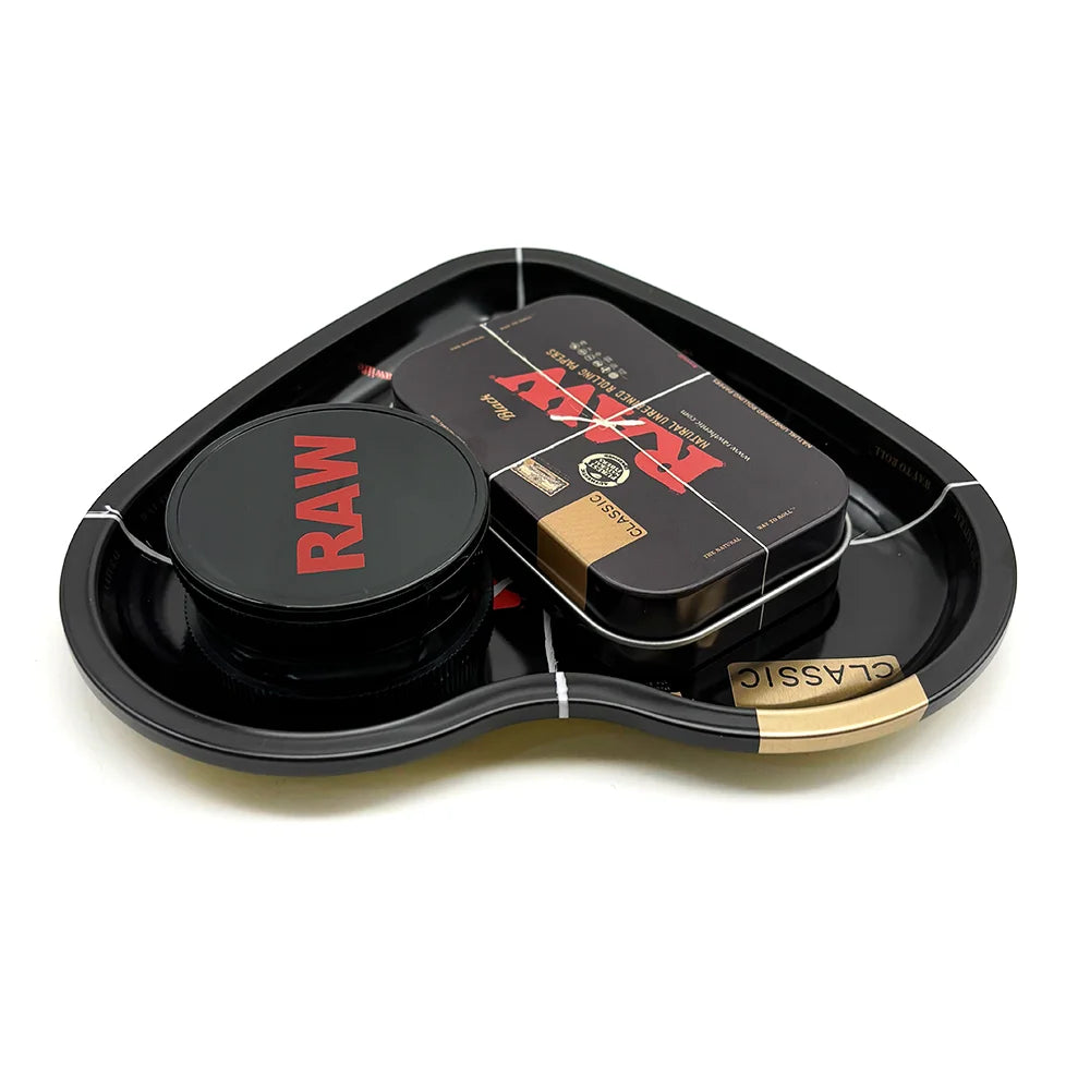 A black love-shaped metal rolling tray holding a dark tin and a rectangular box for a herb grinder.