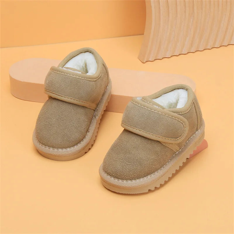 A pair of tan faux leather winter boots for toddlers with a suede upper and fuzzy lining resting on an orange background.