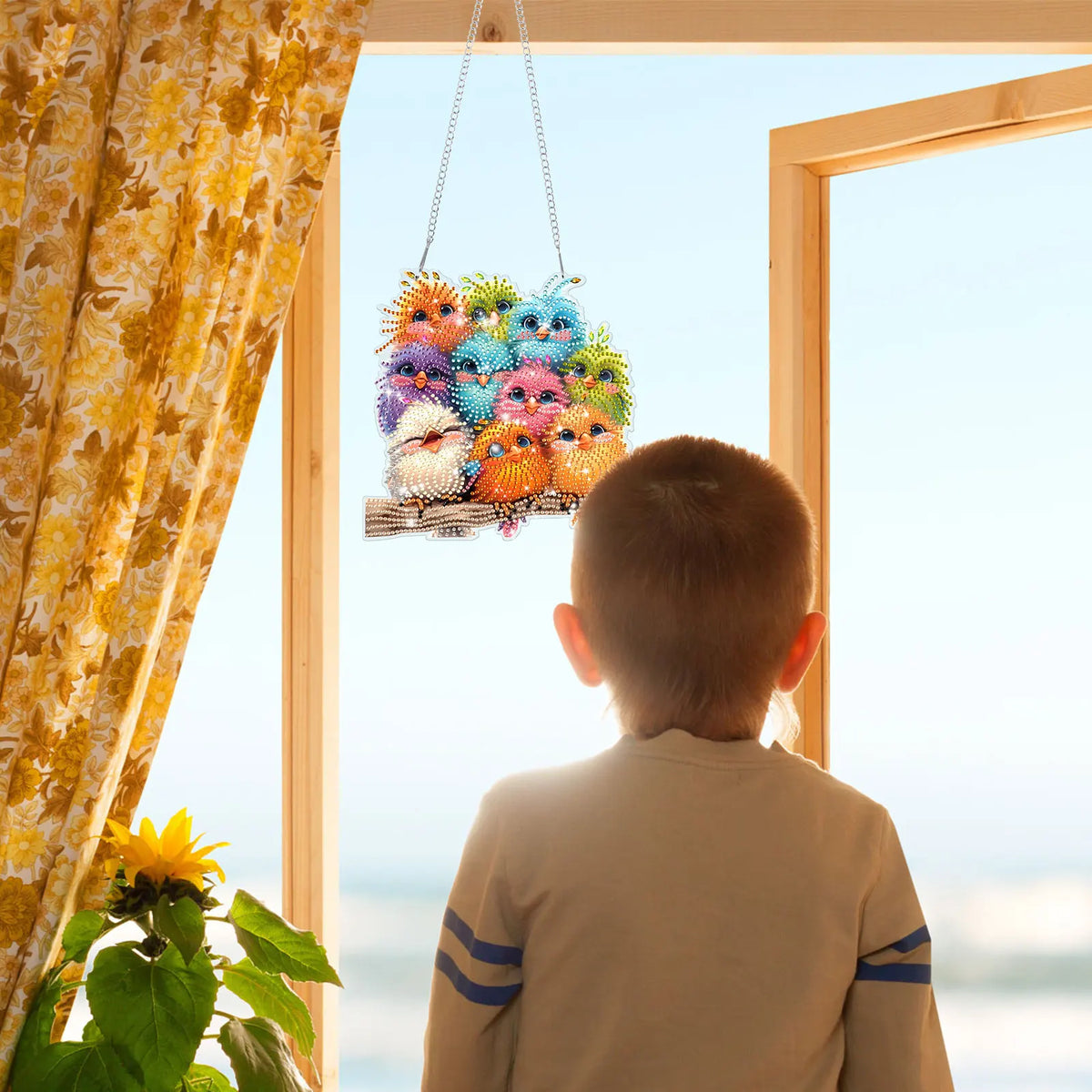 A child looks out a window at a hanging craft of colorful, animal-shaped acrylic pendants.