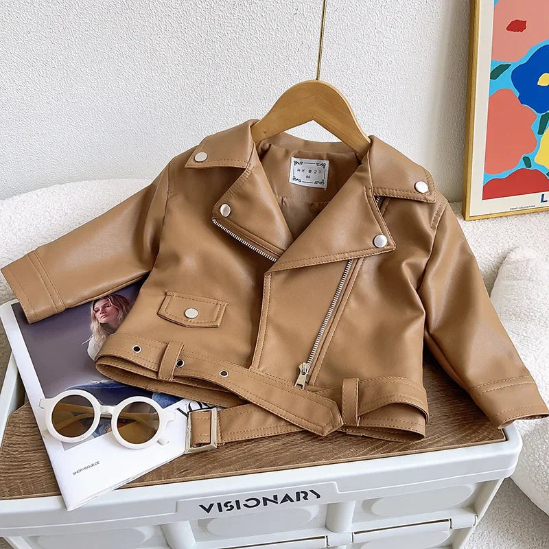 A tan faux leather zip-up jacket displayed on a white storage box with sunglasses and a book.