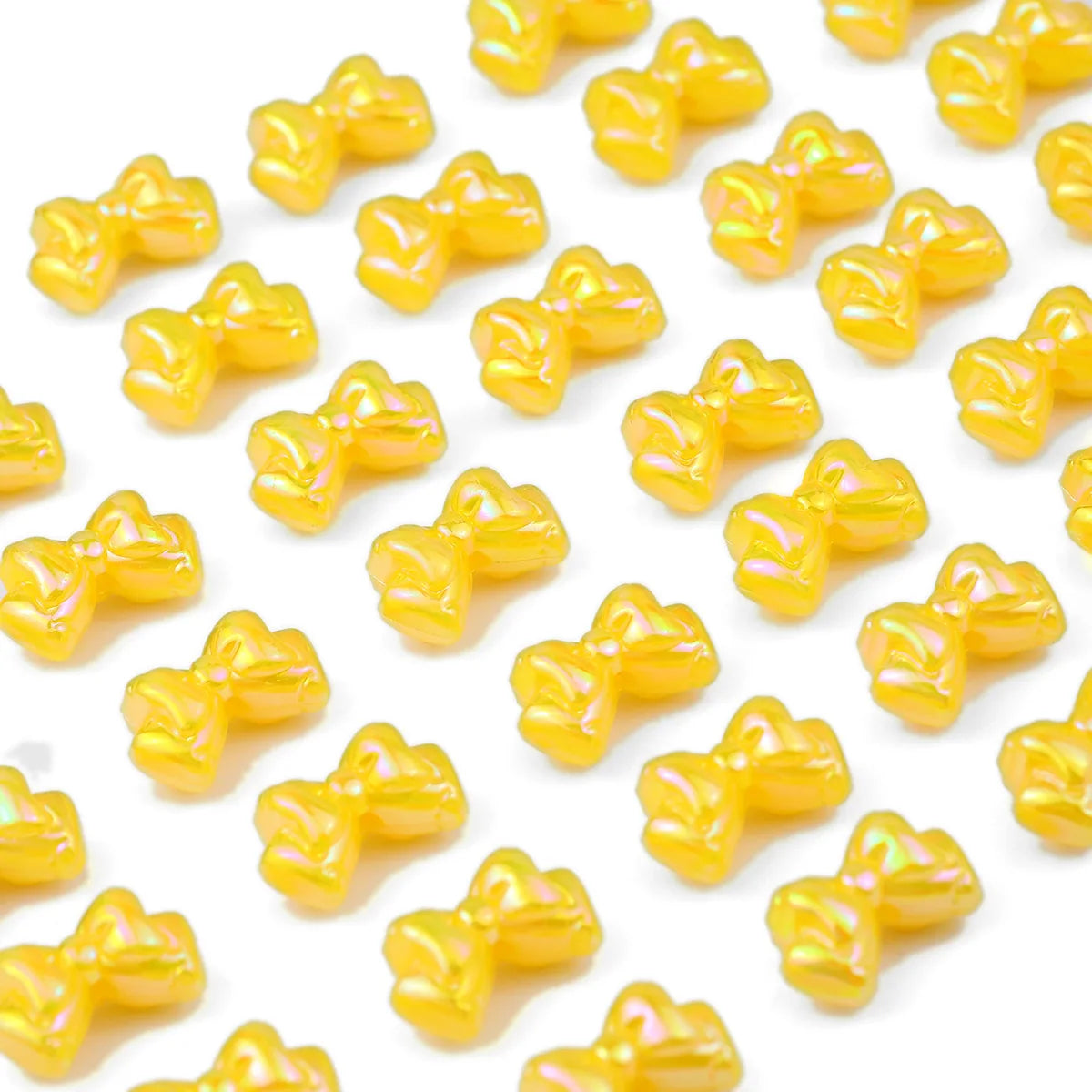 A close-up of small, yellow acrylic bow beads scattered across a white background.