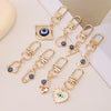 A set of gold-toned evil eye keychains featuring blue and black eyes, displayed on a white background.