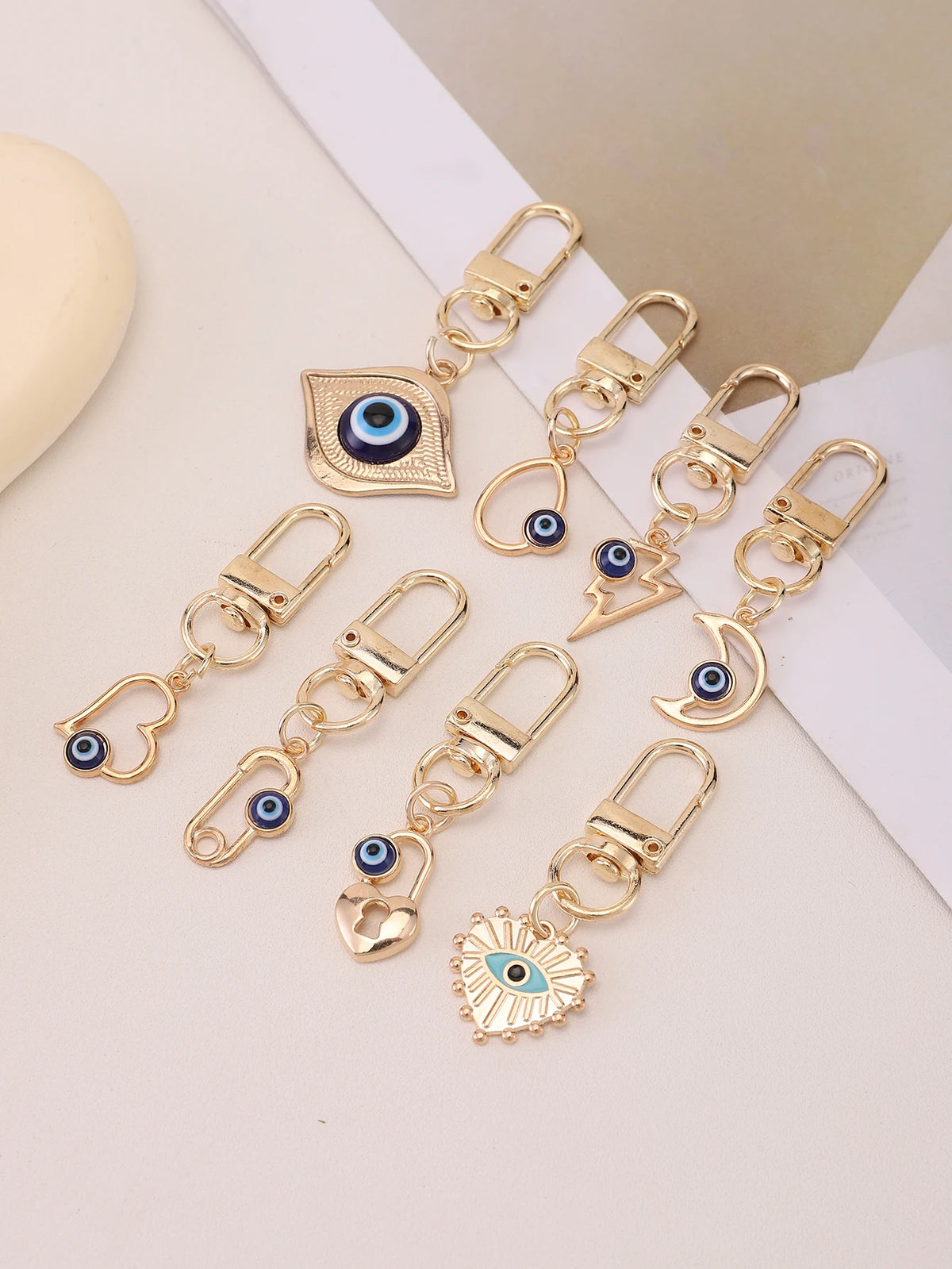 A set of gold-toned evil eye keychains featuring blue and black eyes, displayed on a white background.