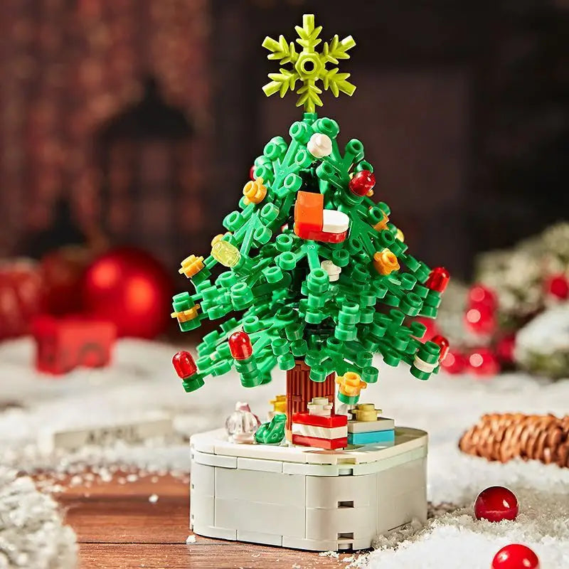 A green Christmas tree built from LEGO bricks with a yellow snowflake topper, resting on a white base covered in snow.