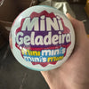A hand holds a spherical toy labeled Mini Geladeira Mini minis minis mini.