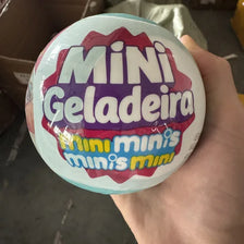 A hand holds a spherical toy labeled Mini Geladeira Mini minis minis mini.
