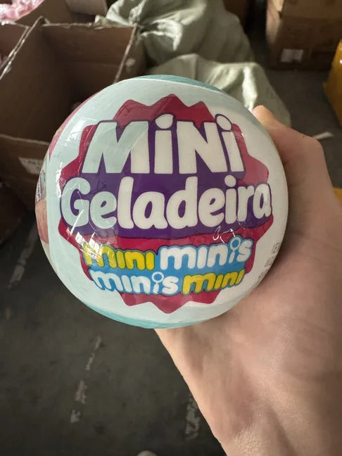 A hand holds a spherical toy labeled Mini Geladeira Mini minis minis mini.