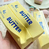 A hand holds two yellow butter squishy toys labeled 4oz salted butter.