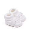 A pair of white knitted baby booties with pink accents and non-slip soles.