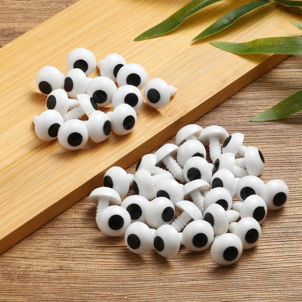 A pile of white and black plastic safety eyes for amigurumi and stuffed animals resting on a wooden board.