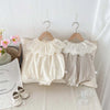 A cream-colored baby girl sleeveless jumpsuit with a lace collar hanging on a wooden hanger against a white background.