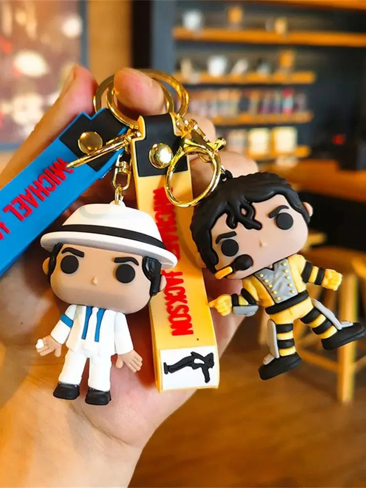 A silicone keychain featuring a figure of Michael Jackson wearing a white hat and striped outfit, attached to a metal clip.