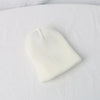 A white knitted baby hat shaped like a cartoon bear resting on a white fabric background.