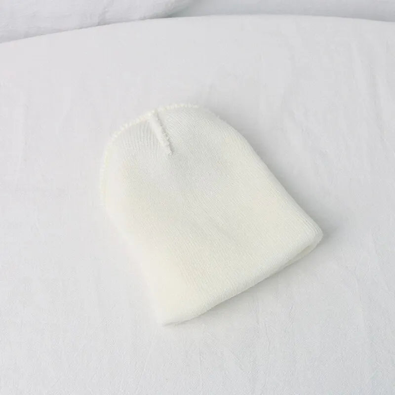 A white knitted baby hat shaped like a cartoon bear resting on a white fabric background.