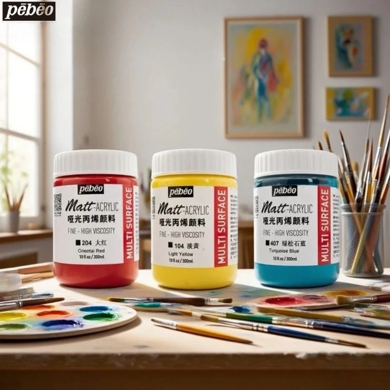 Three bottles of Matte Acrylic Paint in red, yellow, and blue are displayed on a wooden table with paintbrushes.