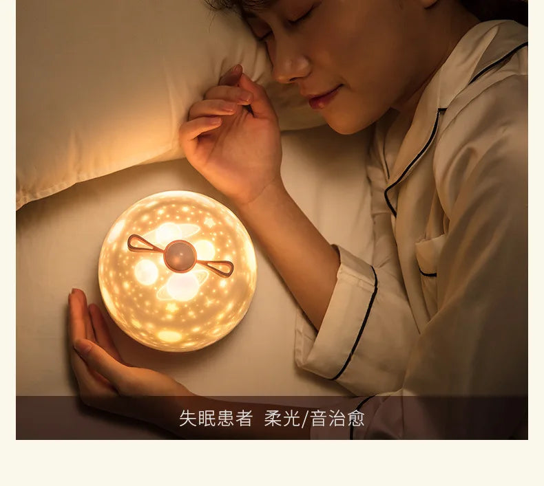 A person is gently holding a round, glowing night light projector with rotating galaxy effects in a soft indoor setting.