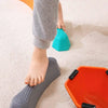 A child's foot is stepping on a gray sensory balance stone, with an orange tray nearby.