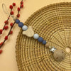 A wooden baby pacifier clip featuring silicone beads in shades of blue and gray, displayed on a woven mat.