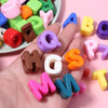 A hand holds various colored acrylic alphabet beads, including letters like A, B, P, and H, for DIY jewelry making.