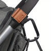 A close-up of heavy-duty stroller hooks with brown leather straps and black grips attached to a gray fabric bag.