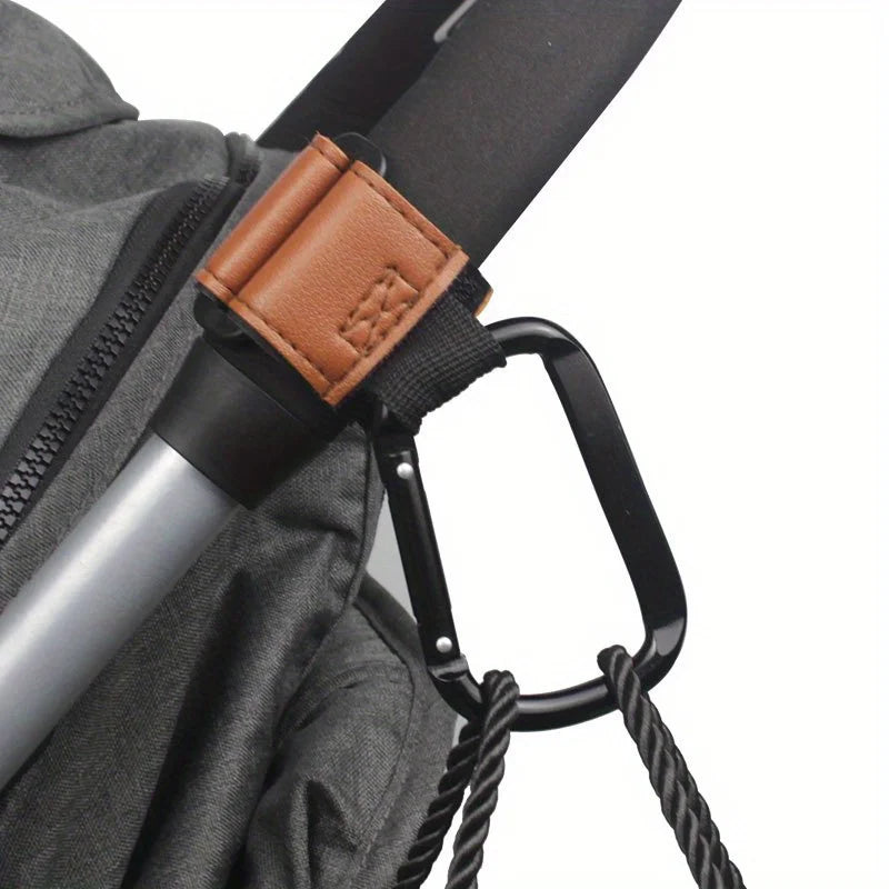 A close-up of heavy-duty stroller hooks with brown leather straps and black grips attached to a gray fabric bag.