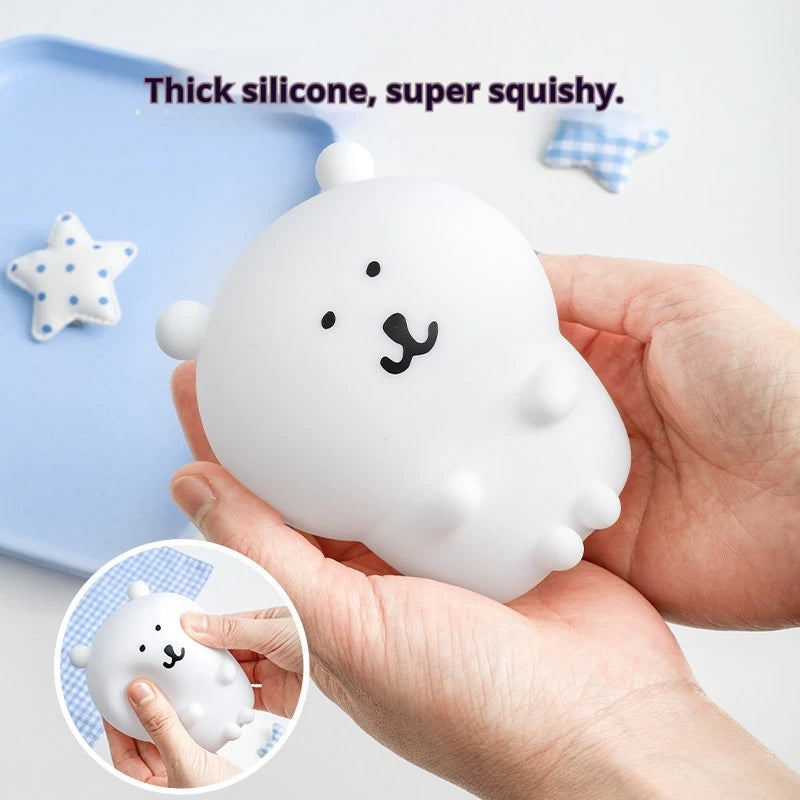A hand holds a white silicone bear lamp against a light blue background.
