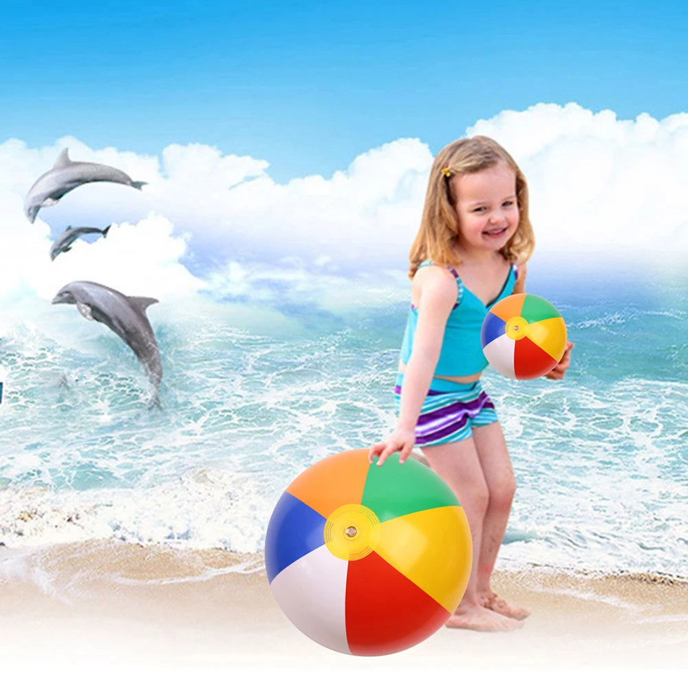 A young girl stands on a beach with six colorful inflatable rainbow balls, and several dolphins are visible in the ocean back