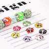 A collection of heart-shaped rhinestone flower charm beads in various shades of green, pink, and yellow are displayed on a wh